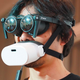 A user with VR glasses over their eyes and the mutalk over their mouth.